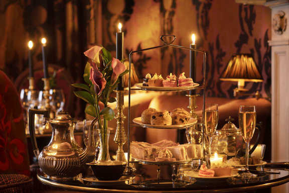 Festive afternoon tea at Prestonfield House, Edinburgh, with a three-tier stand of sandwiches, scones and seasonal pâtisserie set among candlelight, sparkling glassware and rich décor